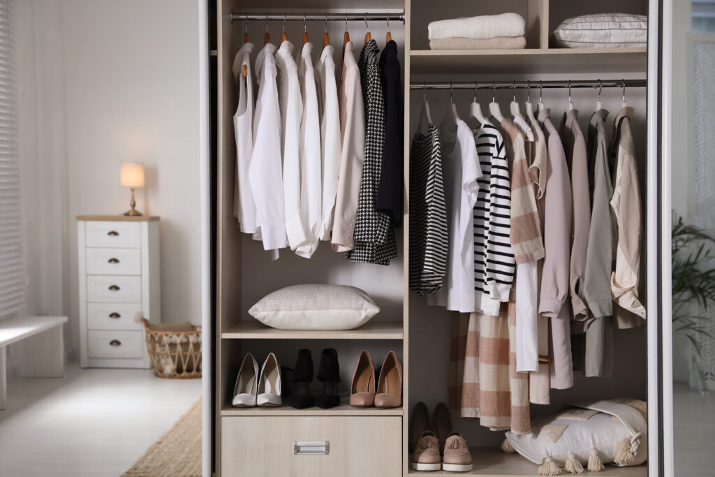 Wardrobe closet with different stylish clothes, shoes and home items in room